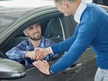 Eine Person in einem blauen Pullover schüttelt die Hand eines Fahrers, der im Auto sitzt, was auf einen Deal oder eine Vereinbarung bei Autoankauf Salzgitter hinweist.