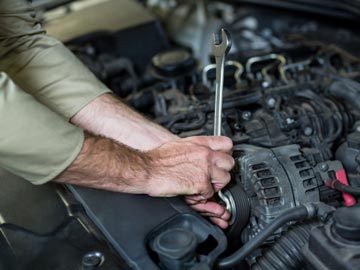 Ein Mechaniker verwendet einen Schraubenschlüssel, um ein Bauteil im Auto-Motor anzuziehen, wobei die Hände bei der Fahrzeugreparatur im Mittelpunkt stehen.