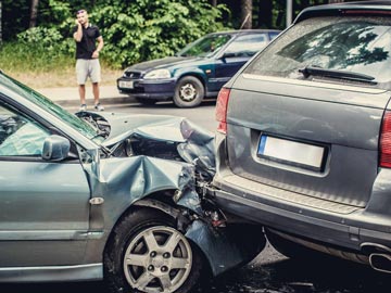 Ein grauer Sedan ist am Heck stark beschädigt, nachdem er mit einem SUV kollidiert ist; ein Mann steht in der Nähe und telefoniert.